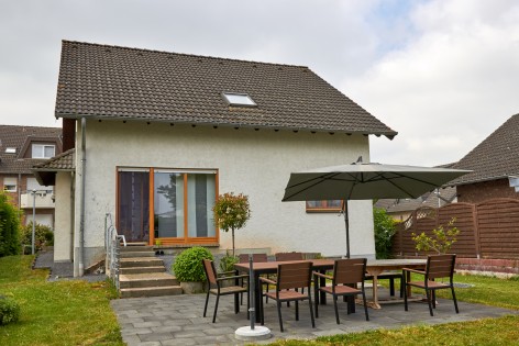 Einfamilienhaus mit weißer Fassade und dunklem Spitzdach und Terrasse mit Sitzecke davor