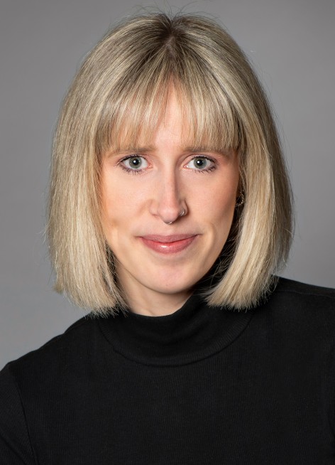 Portraitfoto einer jungen Frau mit blonden, schulterlangen Haaren und Pony